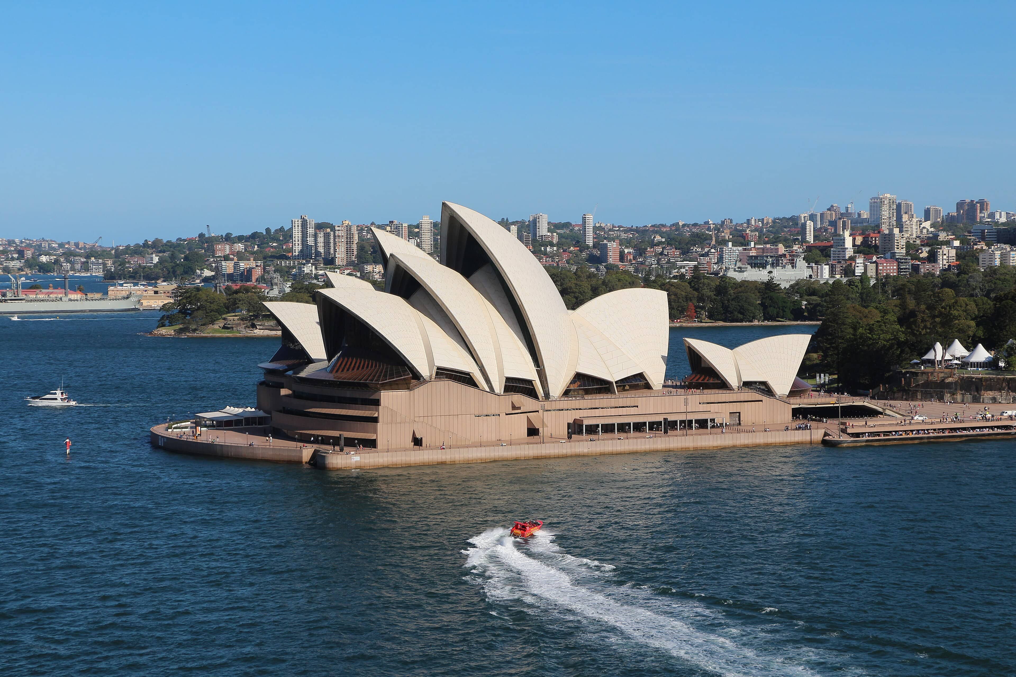 Sydney Opera House gleaming white beside the blue waters of Sydney Harbour on a sunny day.SEP
