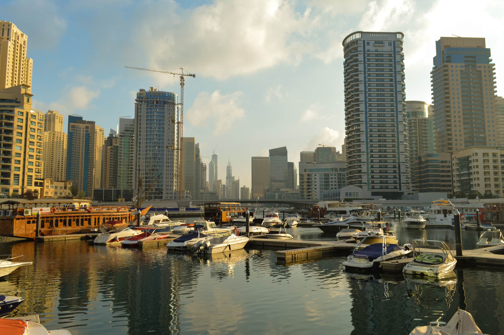 Boats moored at Dubai Marina with sunlit skyscrapers rising behind the waterfront.