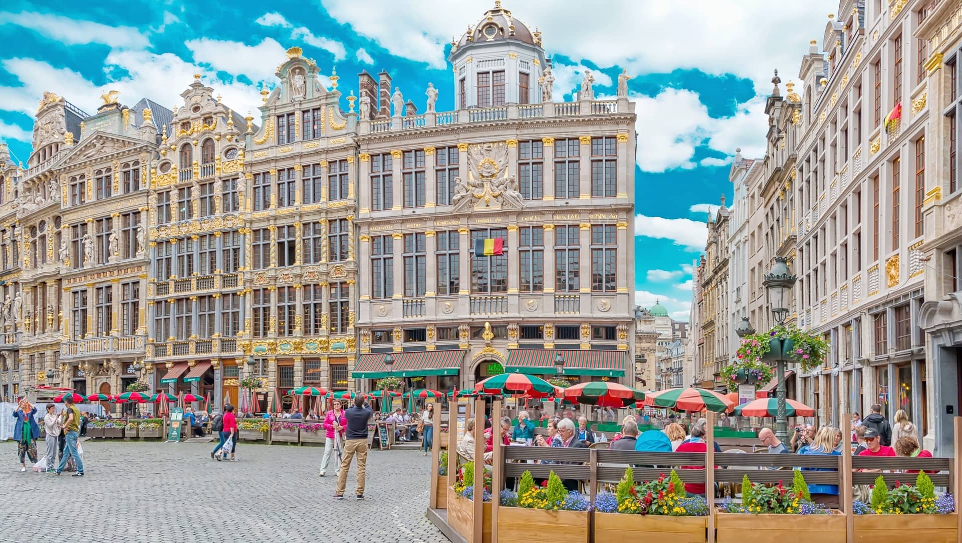 Gilded guildhall façades of Brussels' Grand-Place glowing in bright sunshine against a blue sky.</alt>